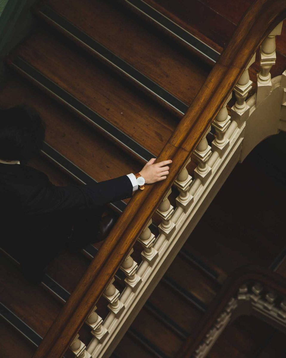 man wearing black suit and watch climbing up wooden stairs